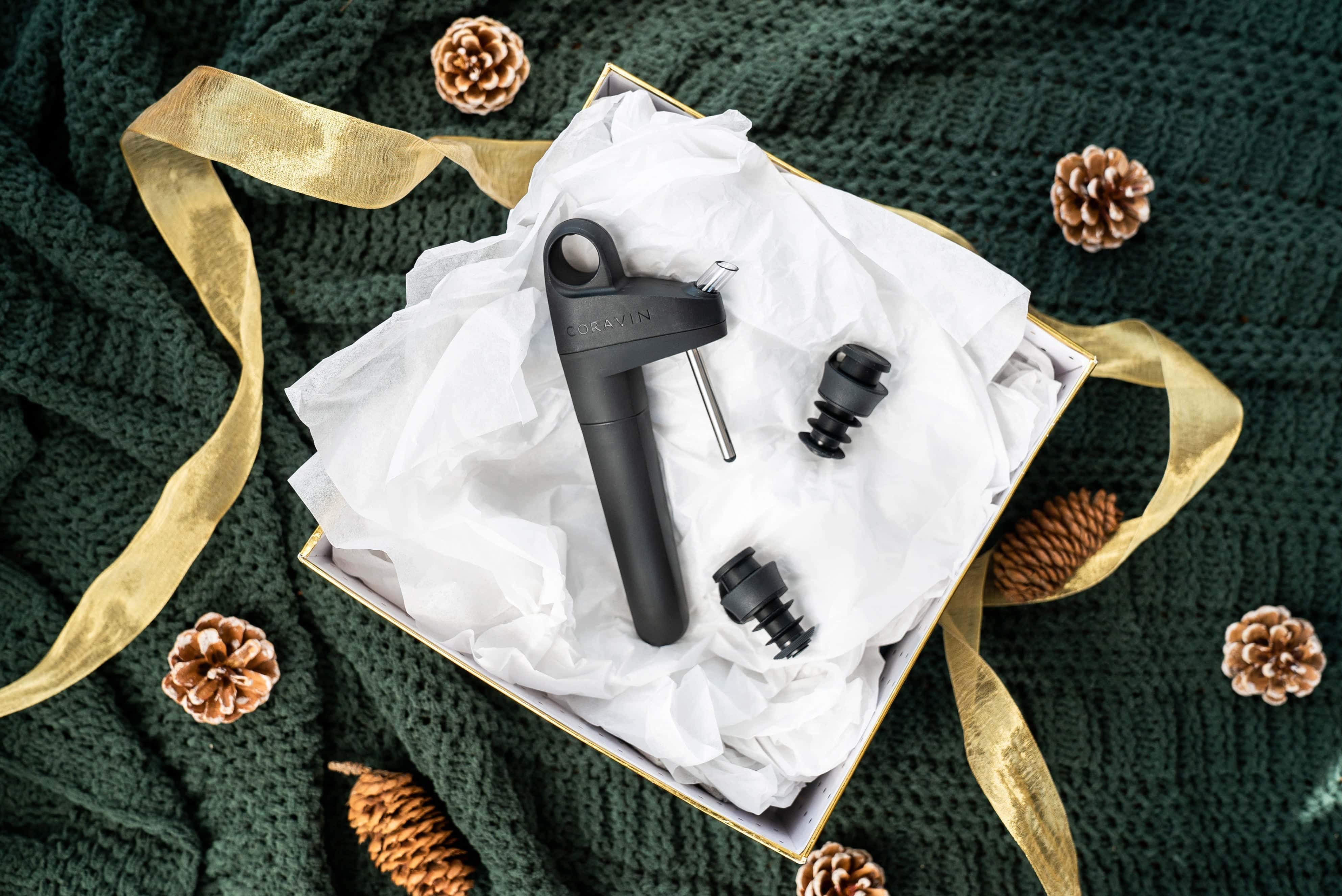 Coravin Pivot wine preservation system elegantly packaged in a gift box with stoppers, displayed on festive green fabric with gold ribbon and pinecones.