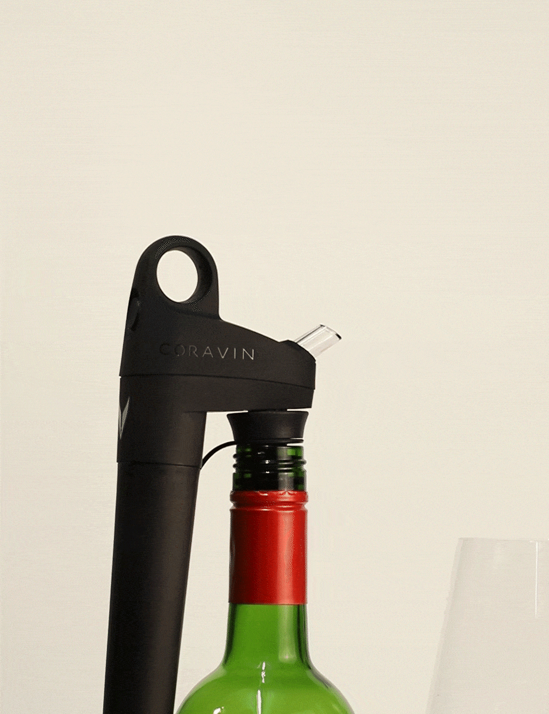 Coravin wine aerator tool on a green wine bottle, with a glass of red wine beside it.