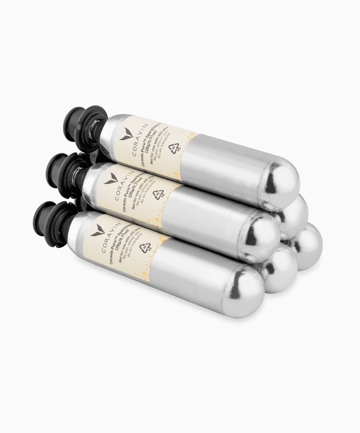 Four Coravin gas cartridges stacked, featuring silver bodies and black tops, with visible branding and usage instructions.