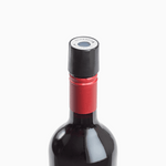 Close-up of a red wine bottle with a black cap and red foil seal, featuring a round label on top.