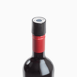 Close-up of a red wine bottle with a black cap and red foil seal, featuring a round label on top.