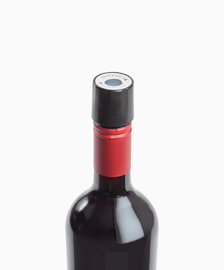 Close-up of a red wine bottle with a black cap and red foil seal, featuring a round label on top.