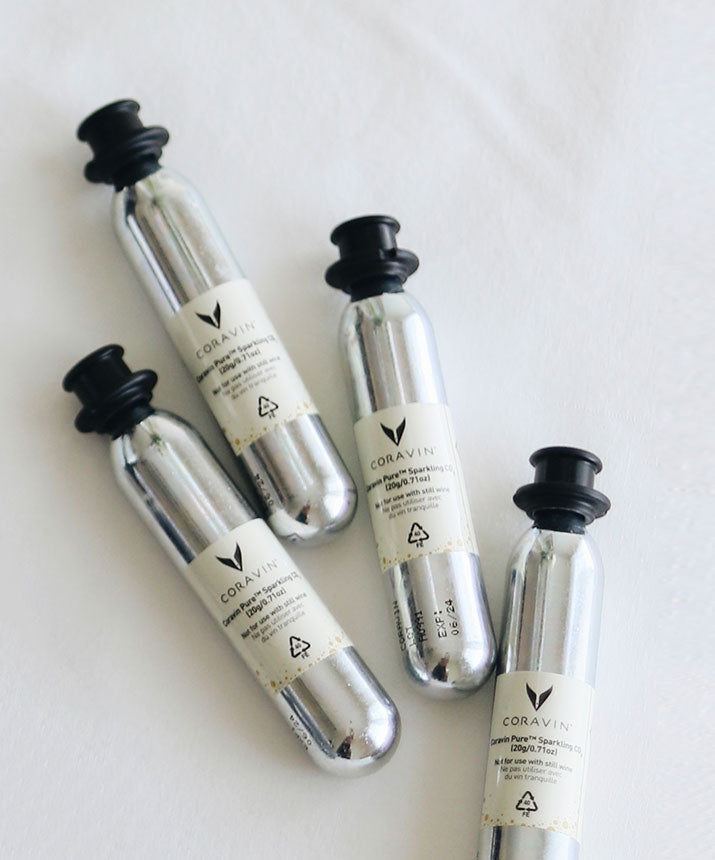 Four silver CO2 canisters labeled "Coravin Pure Sparkling CO2" lying on a white surface.