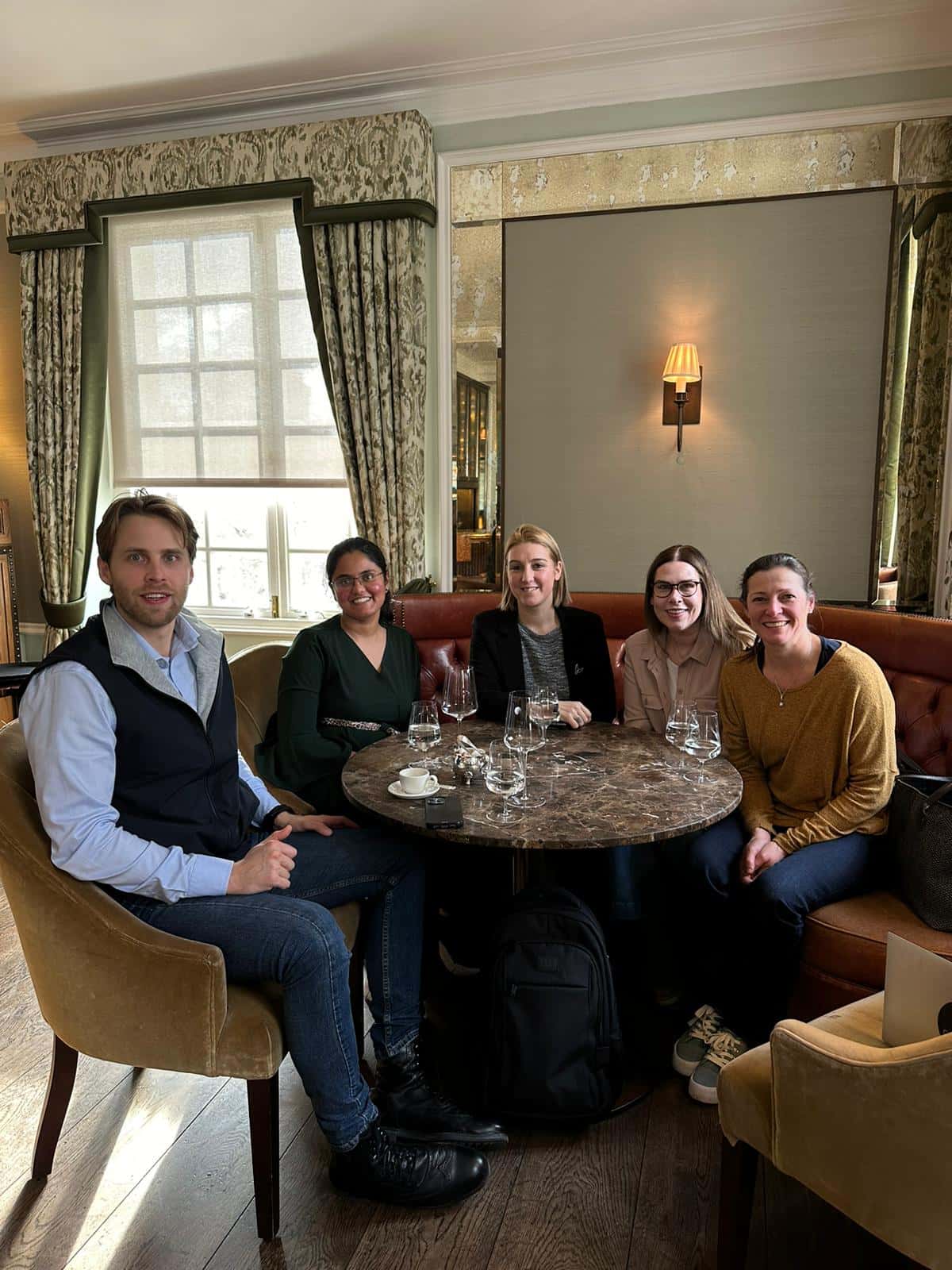 Five people seated around a round table in a cozy restaurant, with wine glasses and a warm interior ambiance.