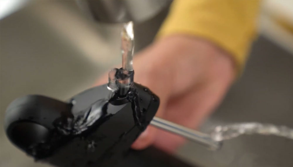 Water flows from a faucet into a black plastic pouring device being held by a person.