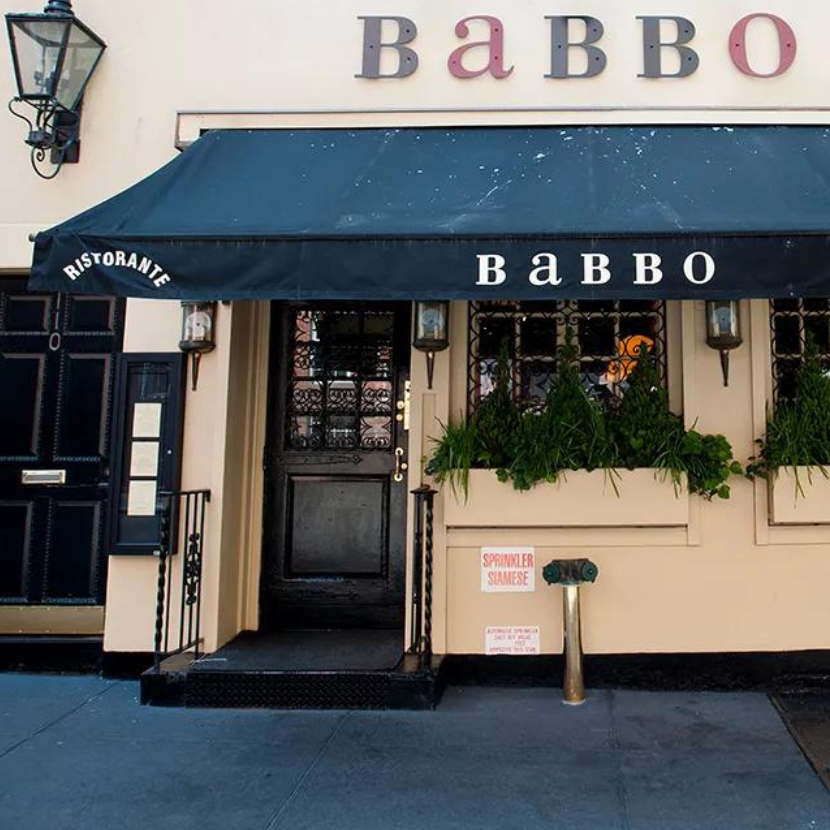 Exterior of Babbo Ristorante with a dark awning, vintage lanterns, and green plants in window boxes along a cream-colored facade.