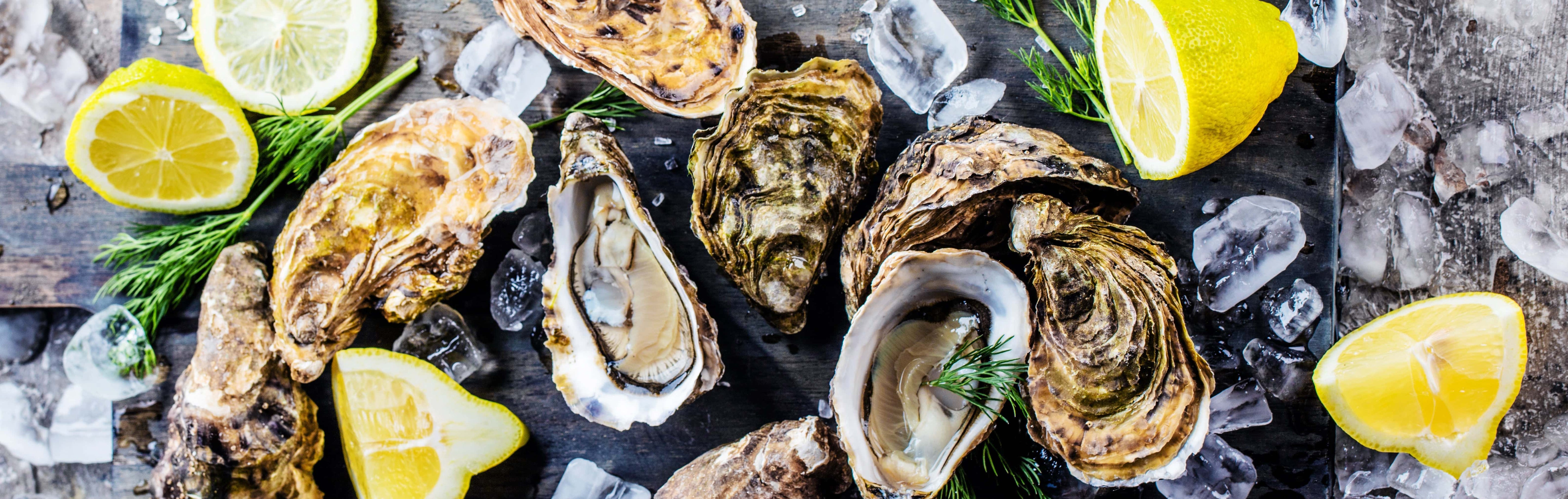 Fresh oysters served on ice with lemon wedges and dill on a rustic wooden platter.