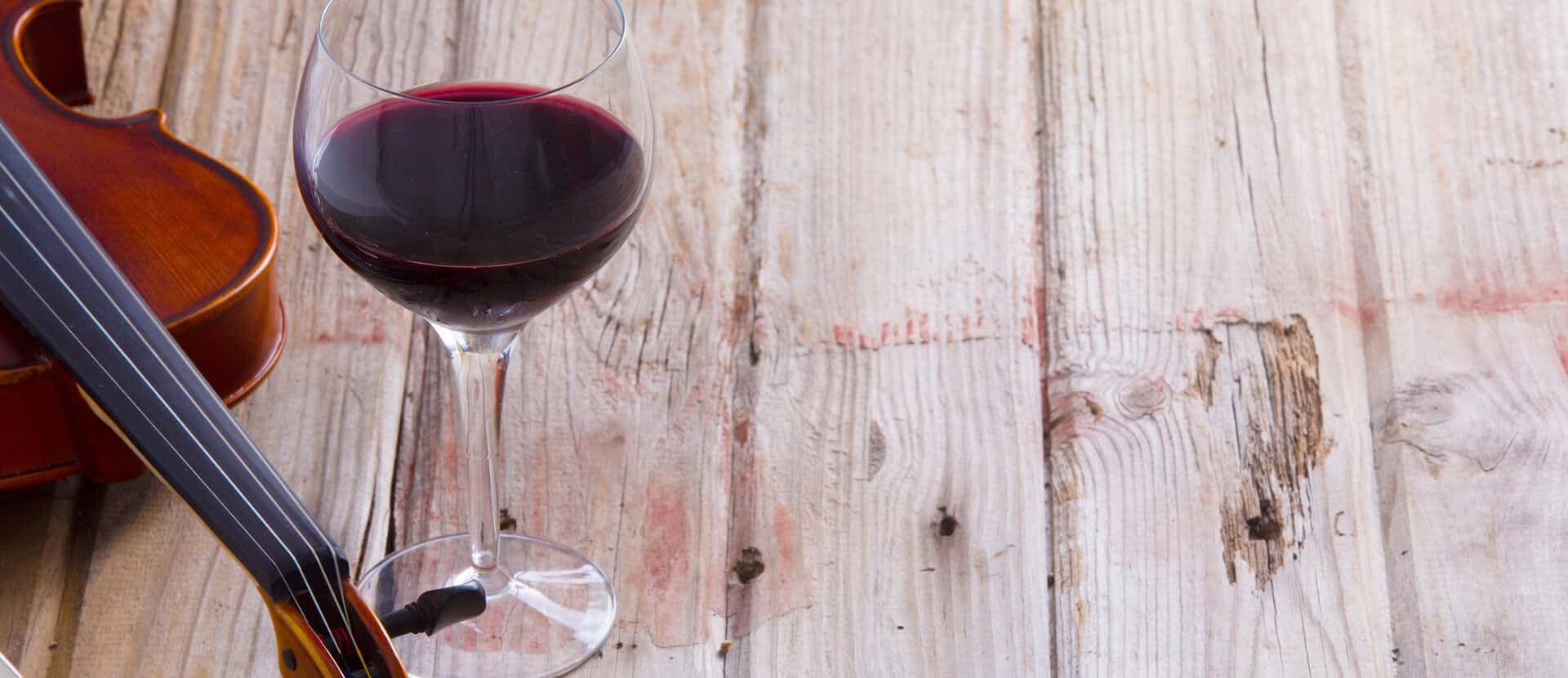 A glass of red wine next to a violin resting on a rustic wooden surface, suggesting a connection between music and wine.