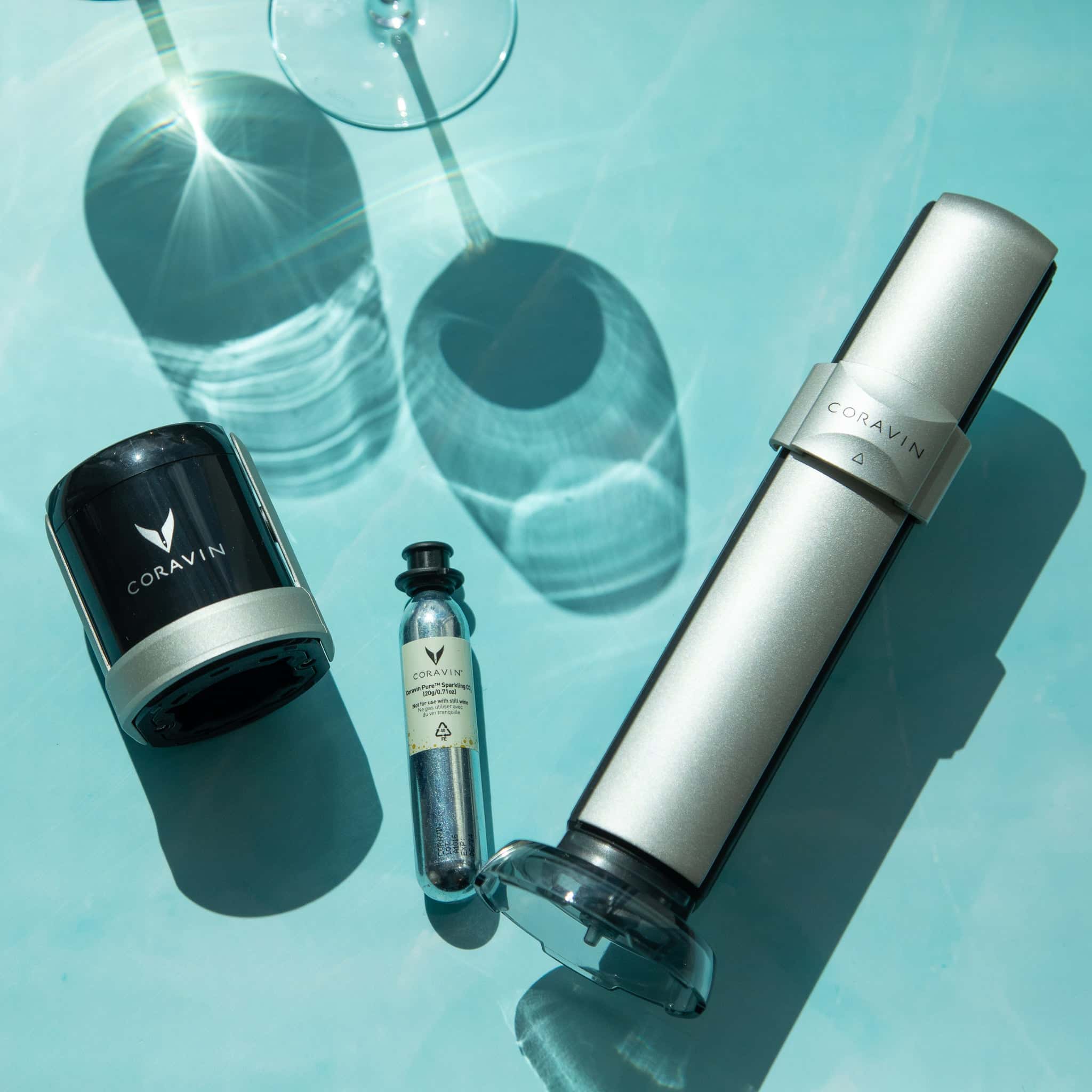 Coravin wine preservation system with sparkling stopper, argon capsule, and wine opener displayed in bright summer sunlight on a turquoise background.